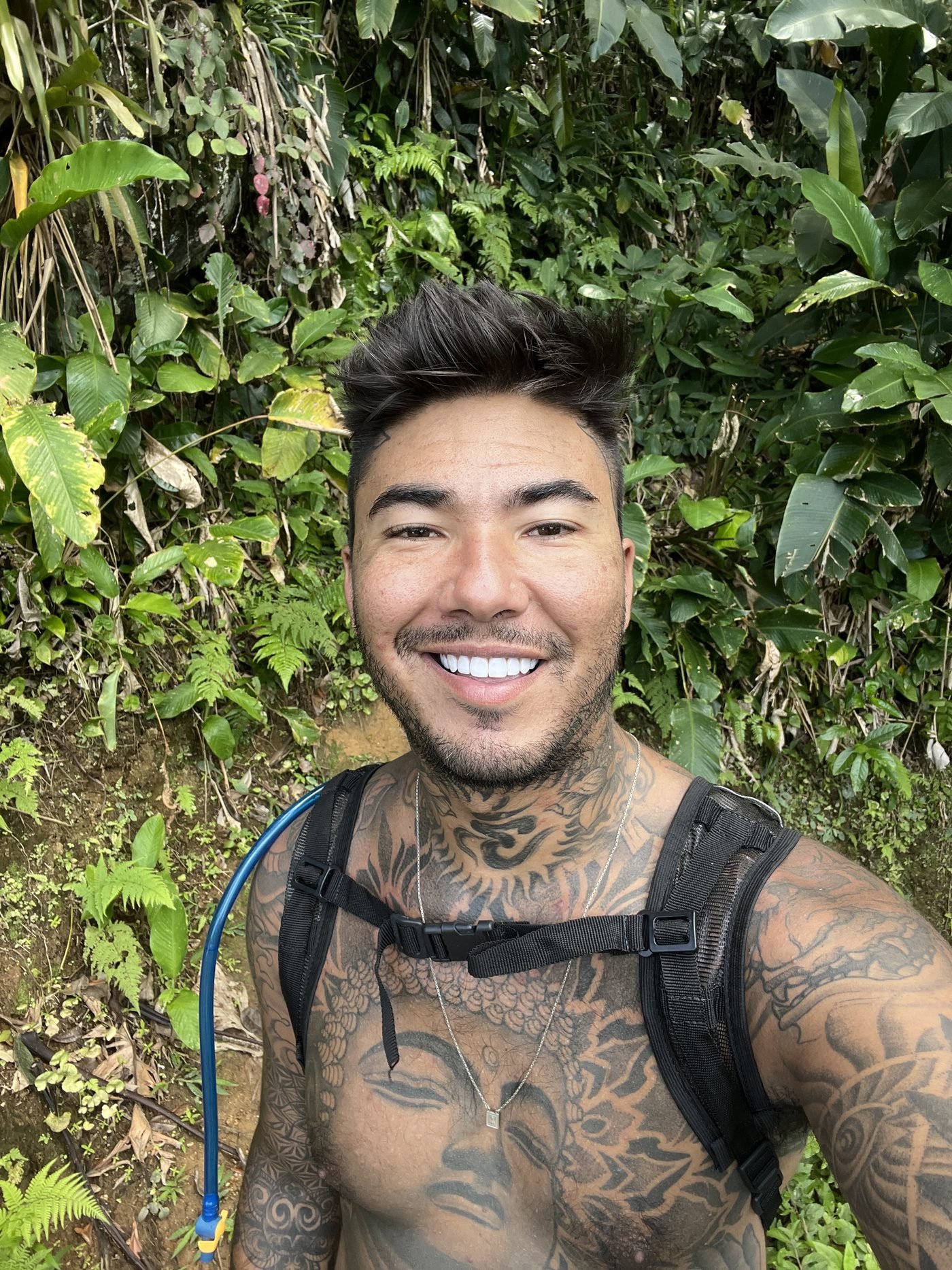 Renan sorrindo na trilha com mochila de hidratação e mata atrás