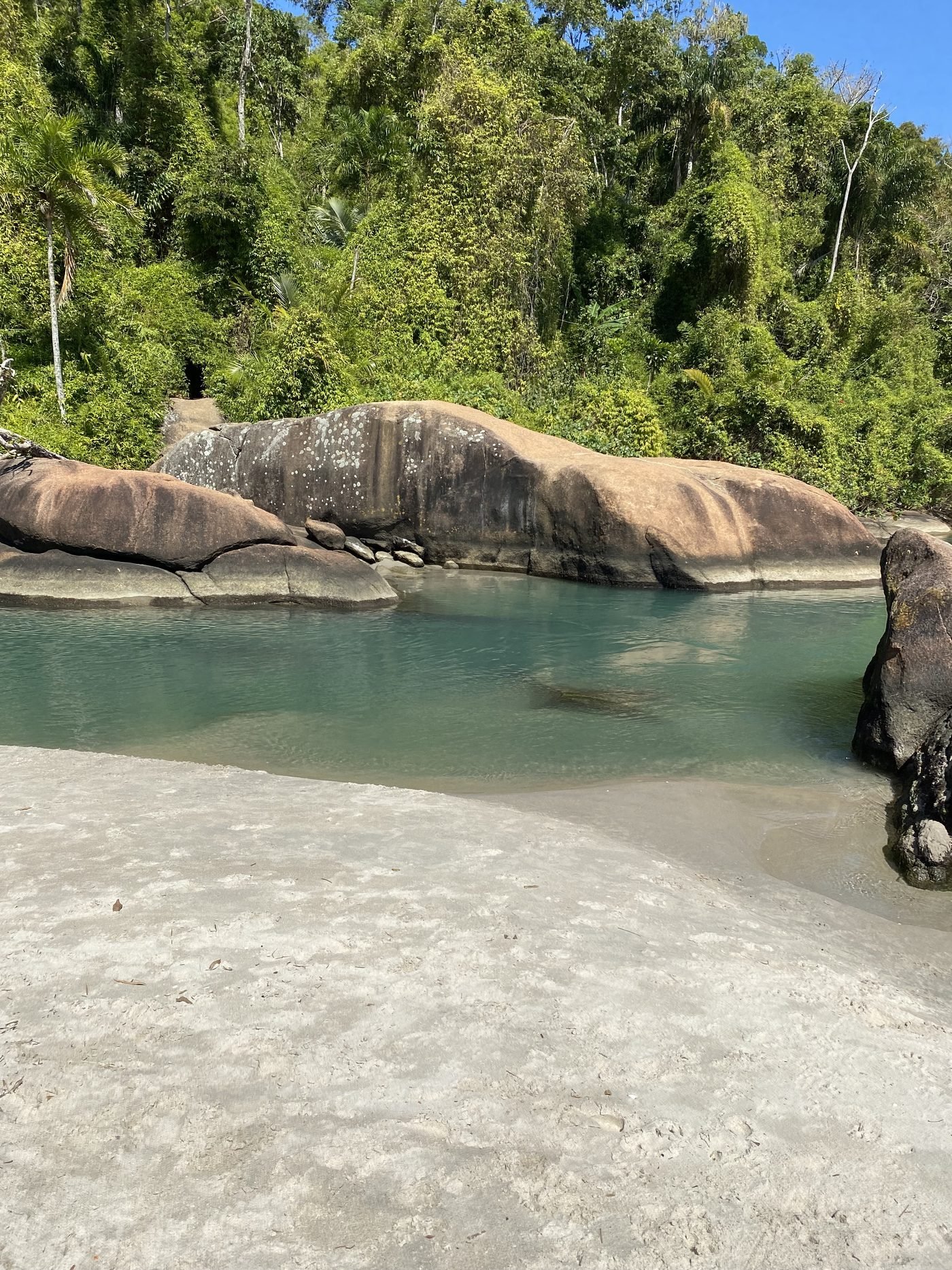 Rio de água clara entre pedras grandes e mata no canto direito da Praia de Itamambuca