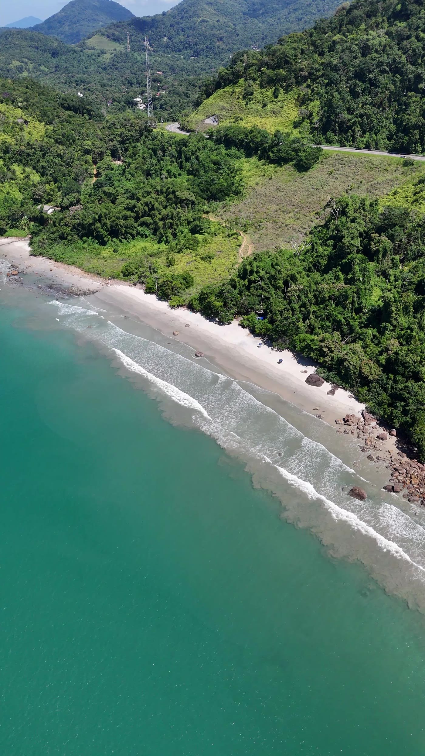 Faixa de areia da Praia do Léo vista de cima, com a estrada passando na encosta