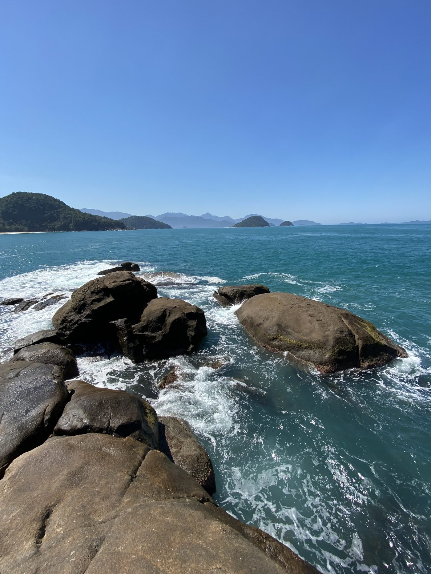 Pedras e mar aberto na Praia do Português, com o horizonte reto e ilhas ao fundo