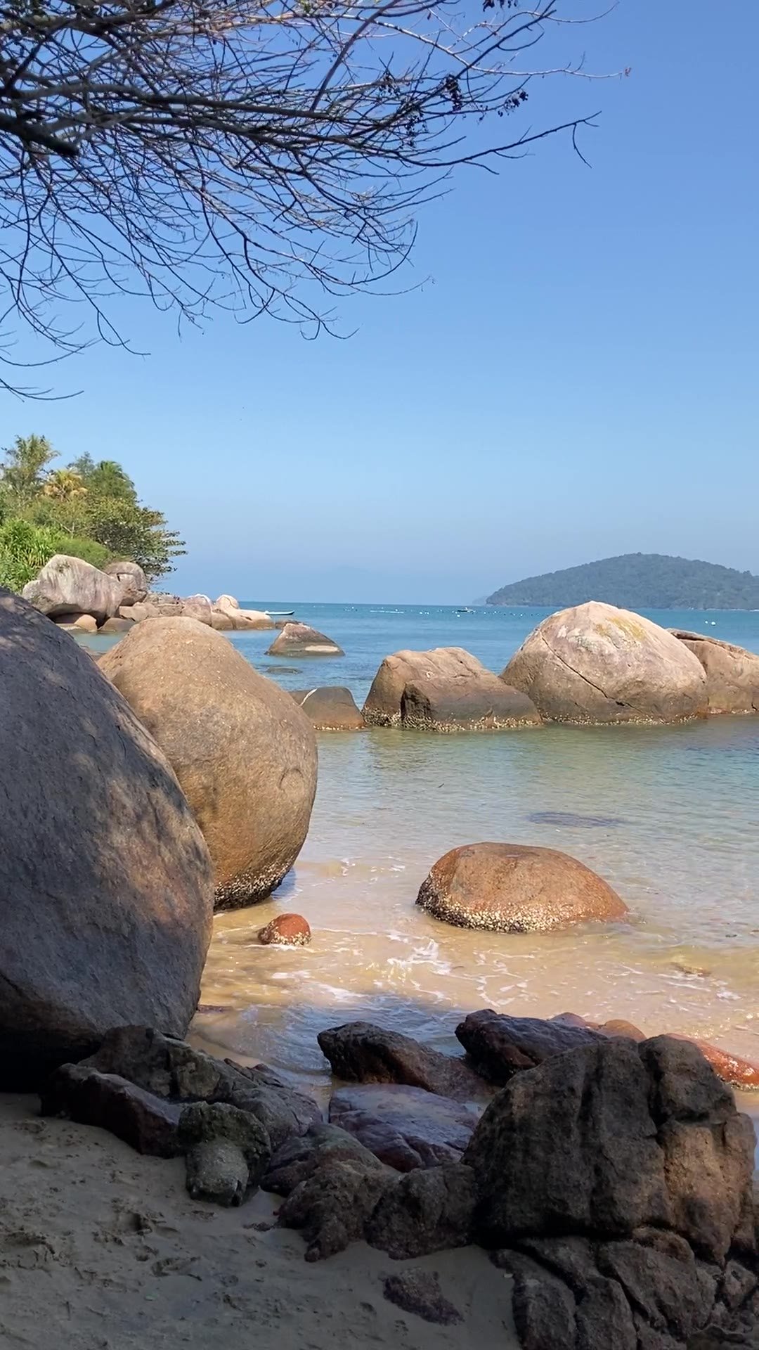 Pedras grandes na areia e mar calmo com ilha ao fundo na região da Enseada