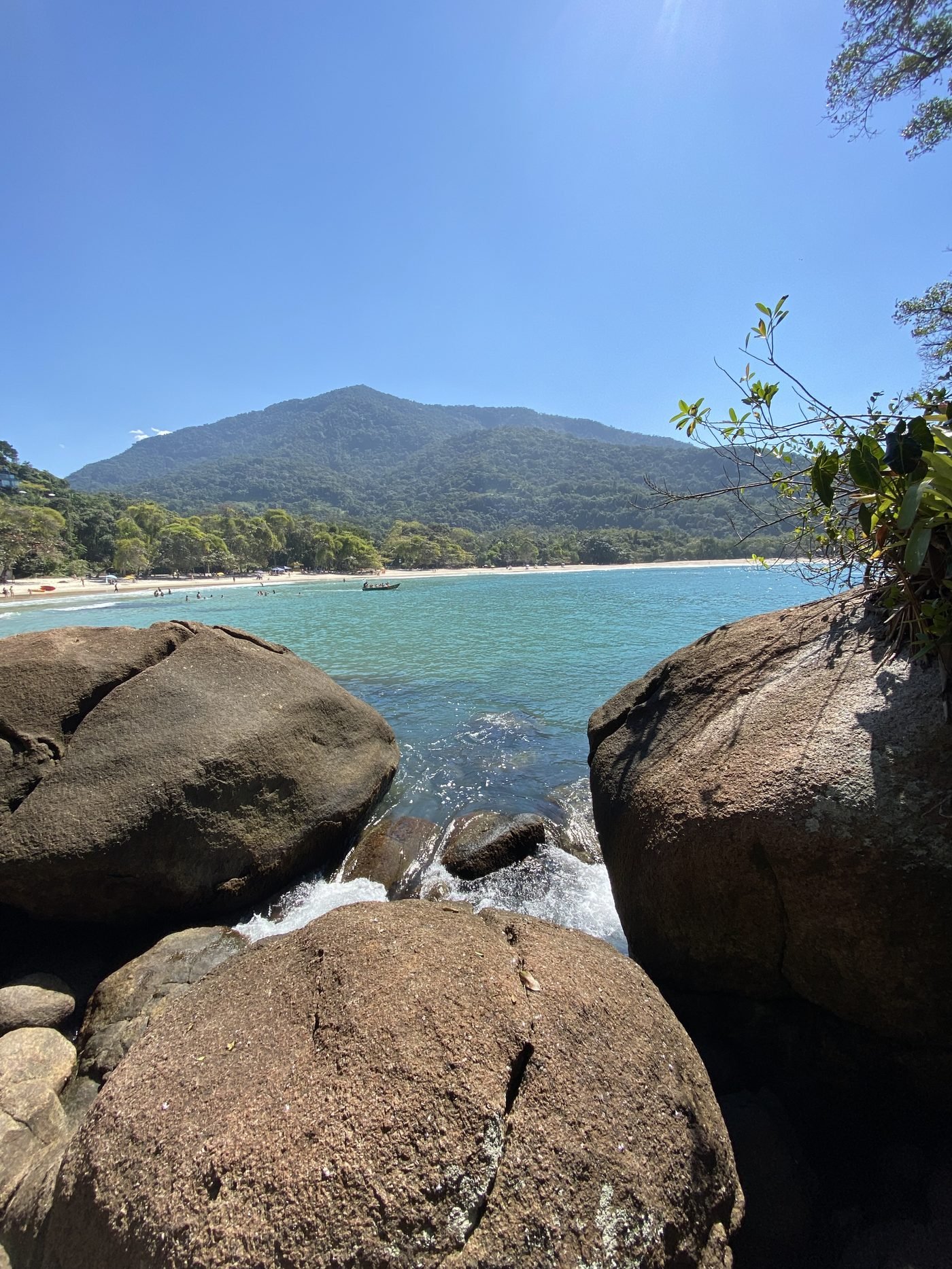 Praia do Félix vista do meio das pedras do costão, com água azul e a serra ao fundo