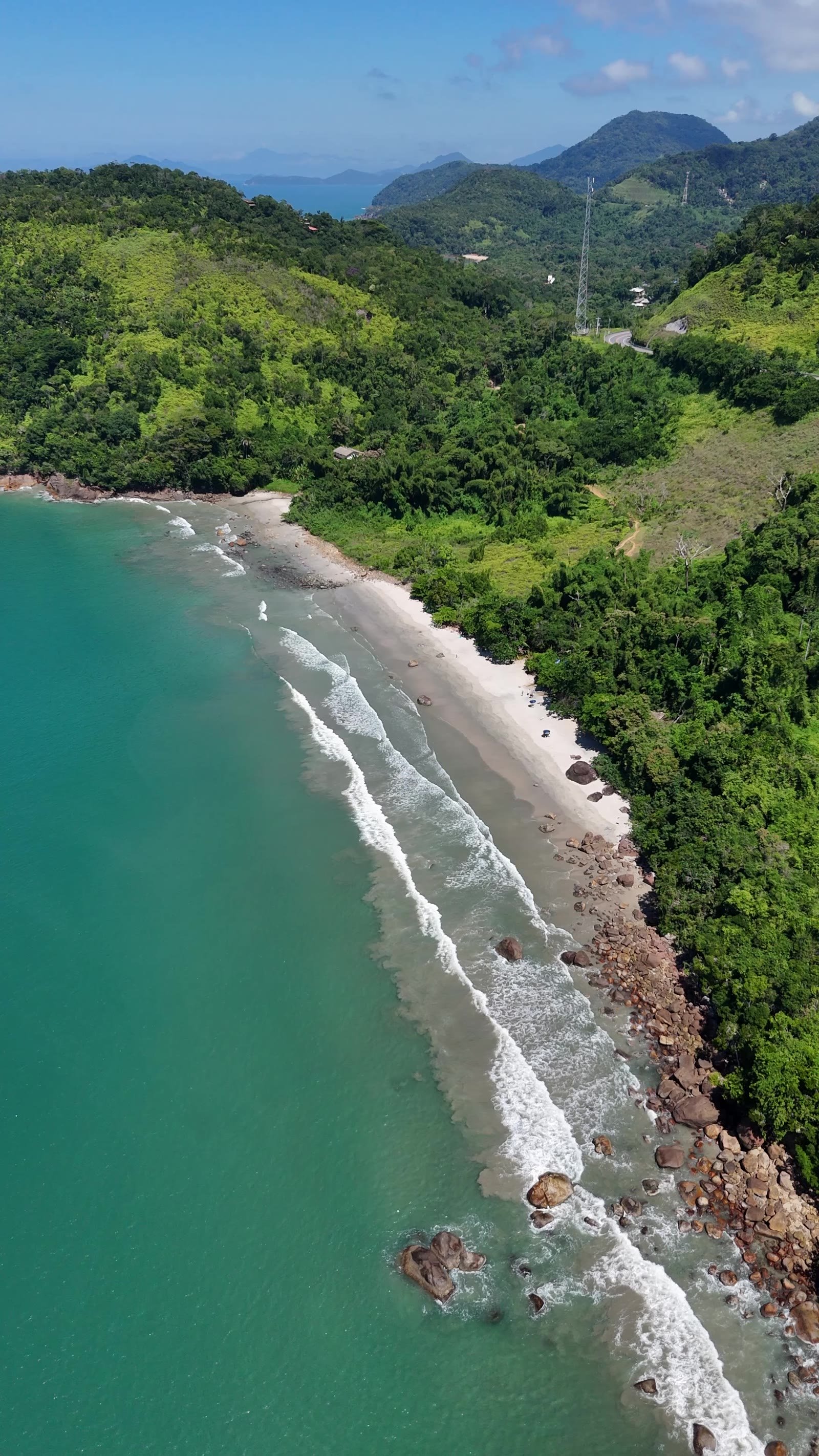 Vista de drone da Praia do Léo, faixa de areia estreita entre a mata e o mar verde, norte de Ubatuba