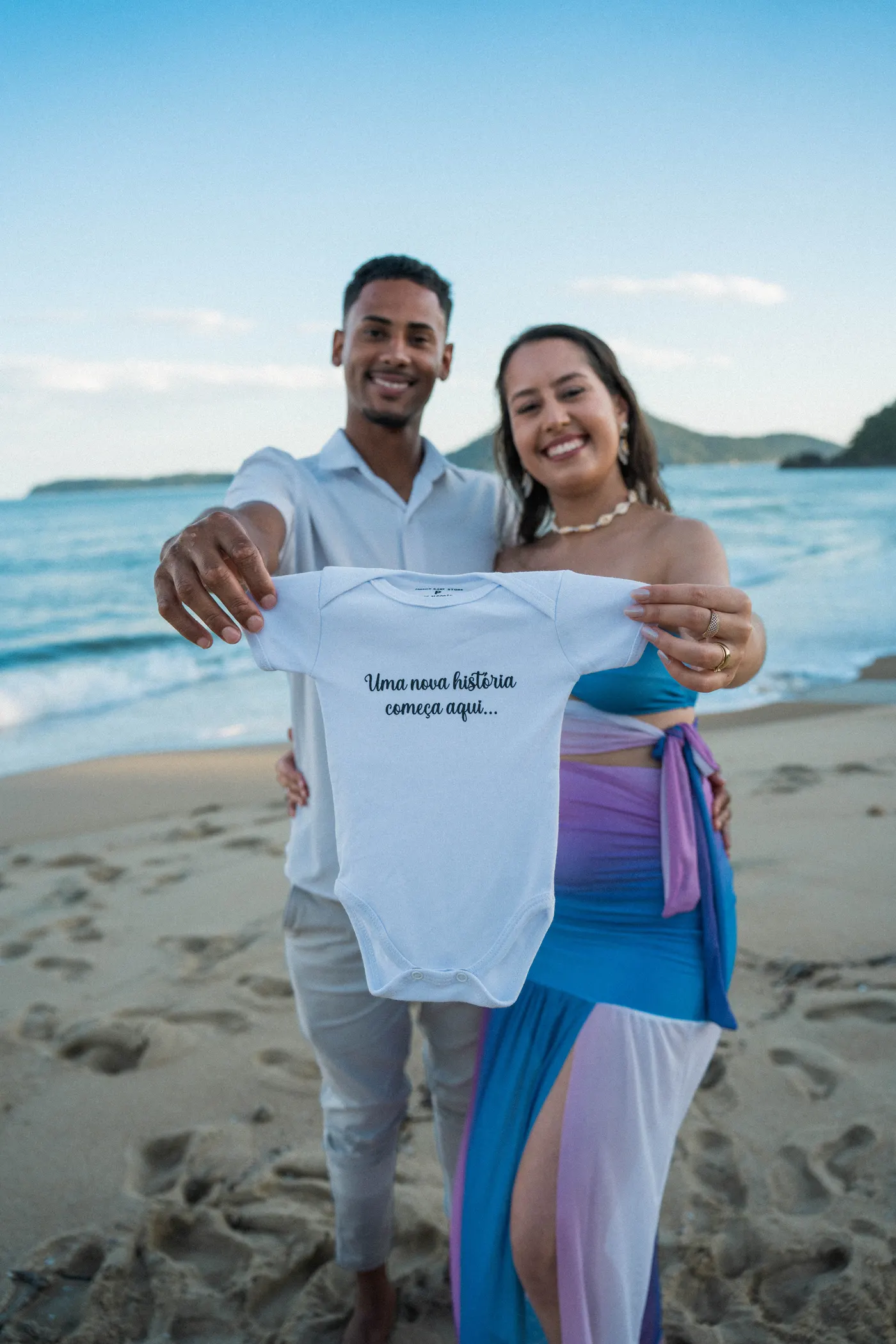 Casal mostrando o body com a frase do bebê — foto autoral de Renan Life, Ubatuba