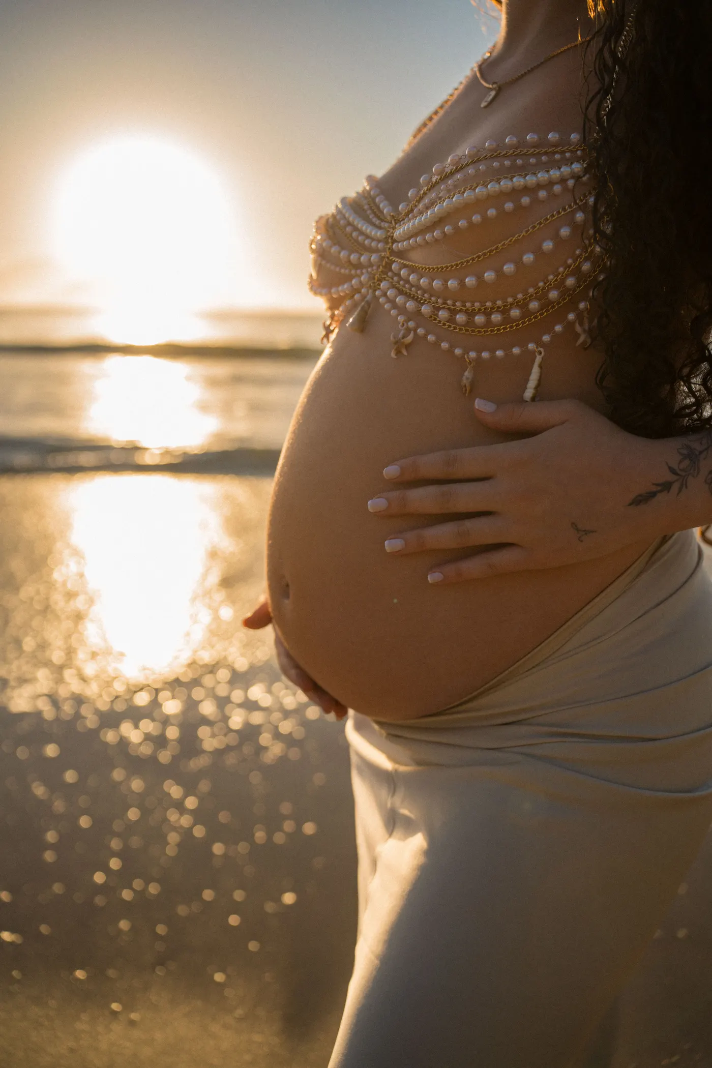 Gestante de perfil com as mãos na barriga e o sol atrás — foto autoral de Renan Life, Ubatuba