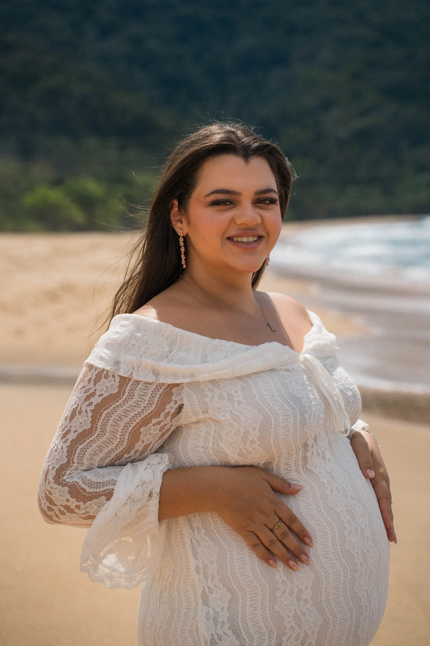 Gestante sorrindo com a mão na barriga na praia — foto autoral de Renan Life, Ubatuba