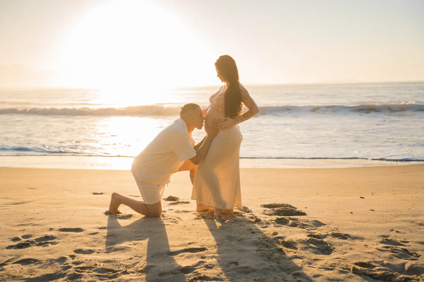 Parceiro ajoelhado beijando a barriga contra o sol — foto autoral de Renan Life, Ubatuba