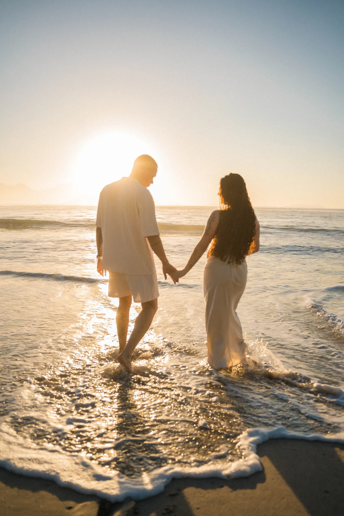 Casal de mãos dadas entrando no mar com o sol à frente — foto autoral de Renan Life, Ubatuba