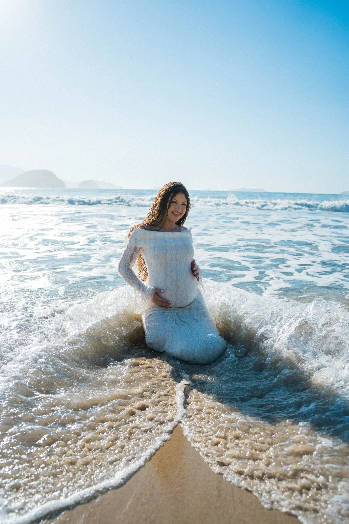 Gestante sentada na beira do mar com a espuma da onda em volta — foto autoral de Renan Life, Ubatuba