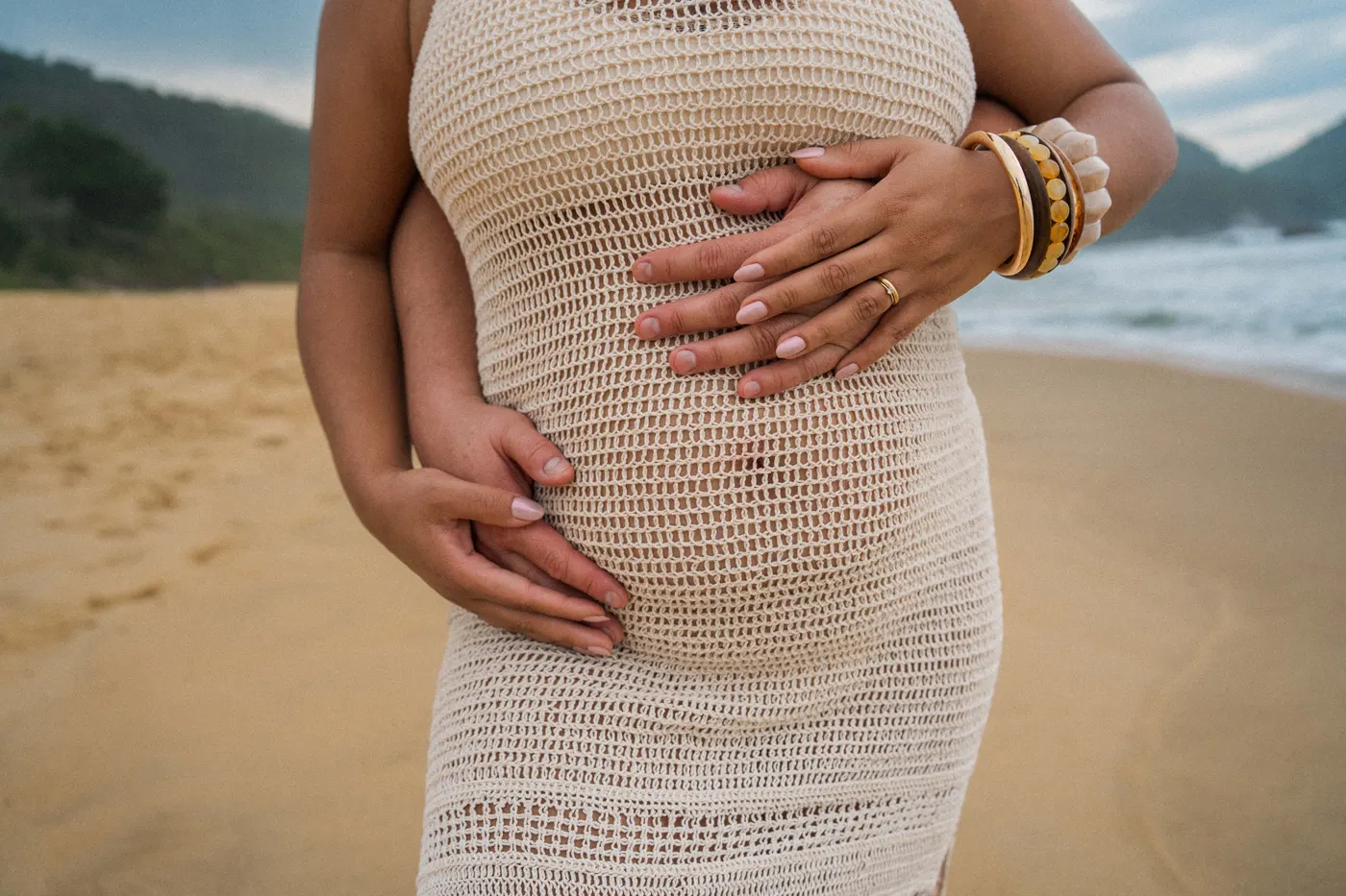 Detalhe das mãos do casal sobre a barriga — foto autoral de Renan Life, Ubatuba