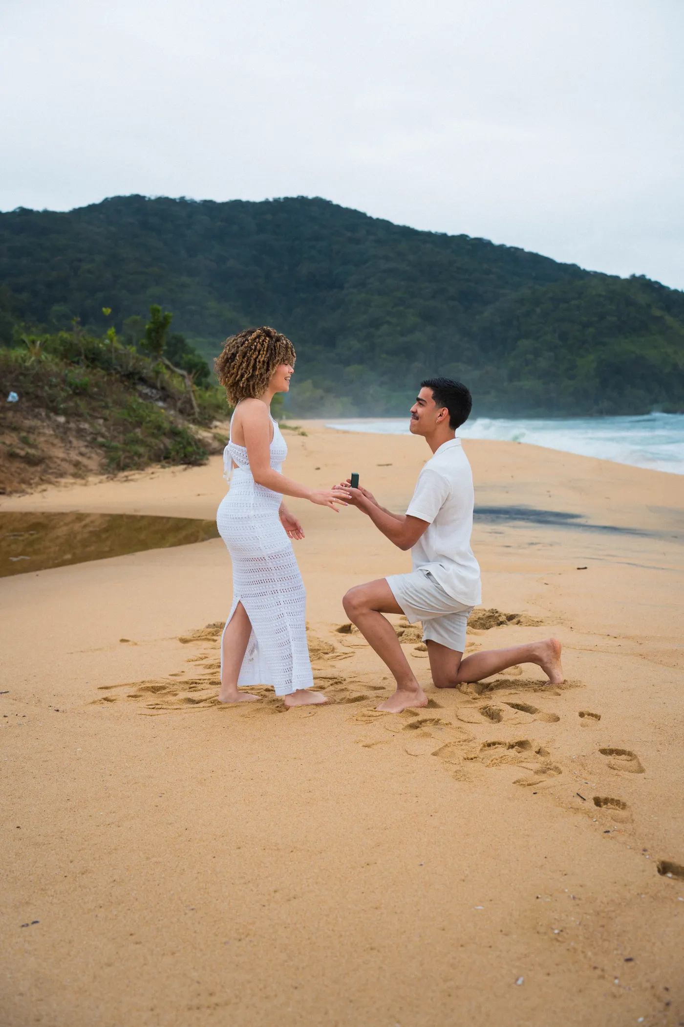Pedido de casamento ajoelhado na areia, com o mar e a mata ao fundo — foto autoral de Renan Life, Ubatuba