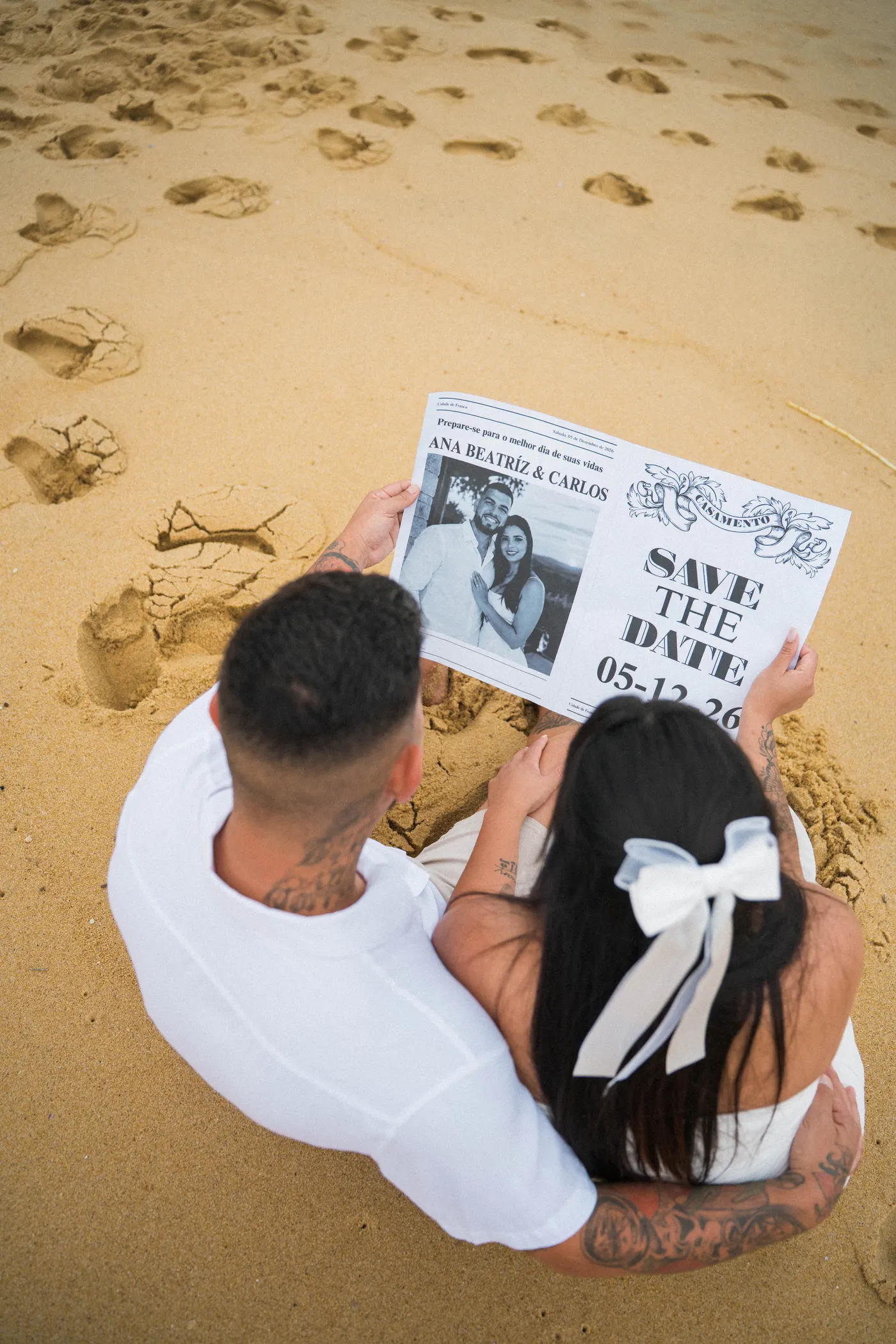 O jornal do save the date visto de cima, com os noivos abraçados — foto autoral de Renan Life, Ubatuba