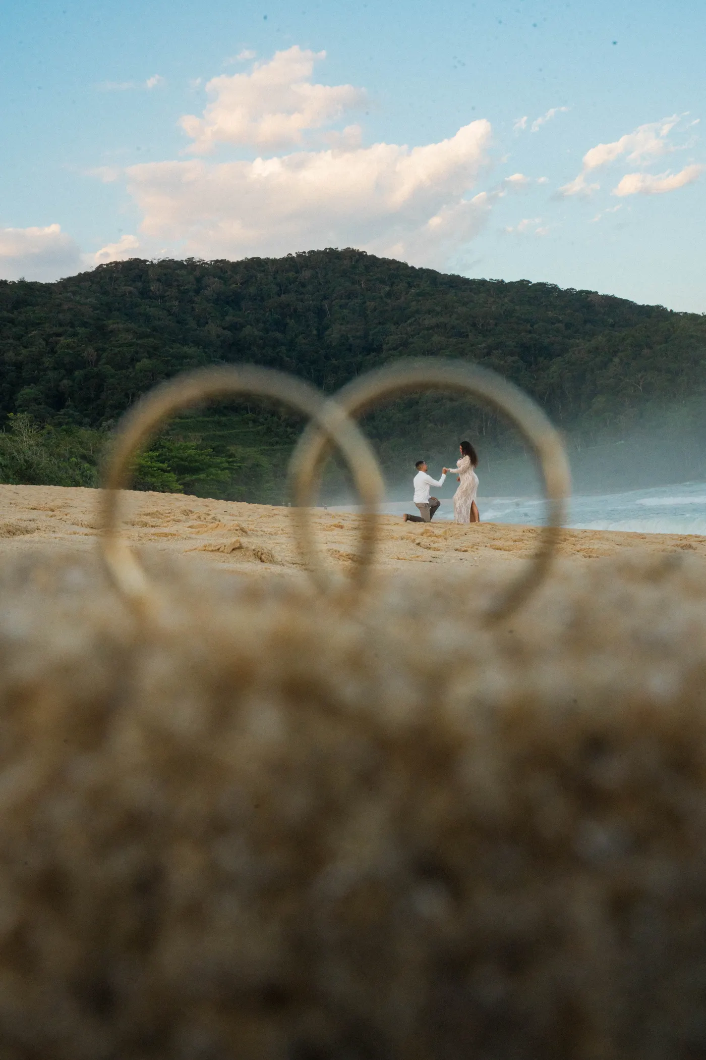 Alianças na areia em primeiro plano e o casal ao fundo — foto autoral de Renan Life, Ubatuba