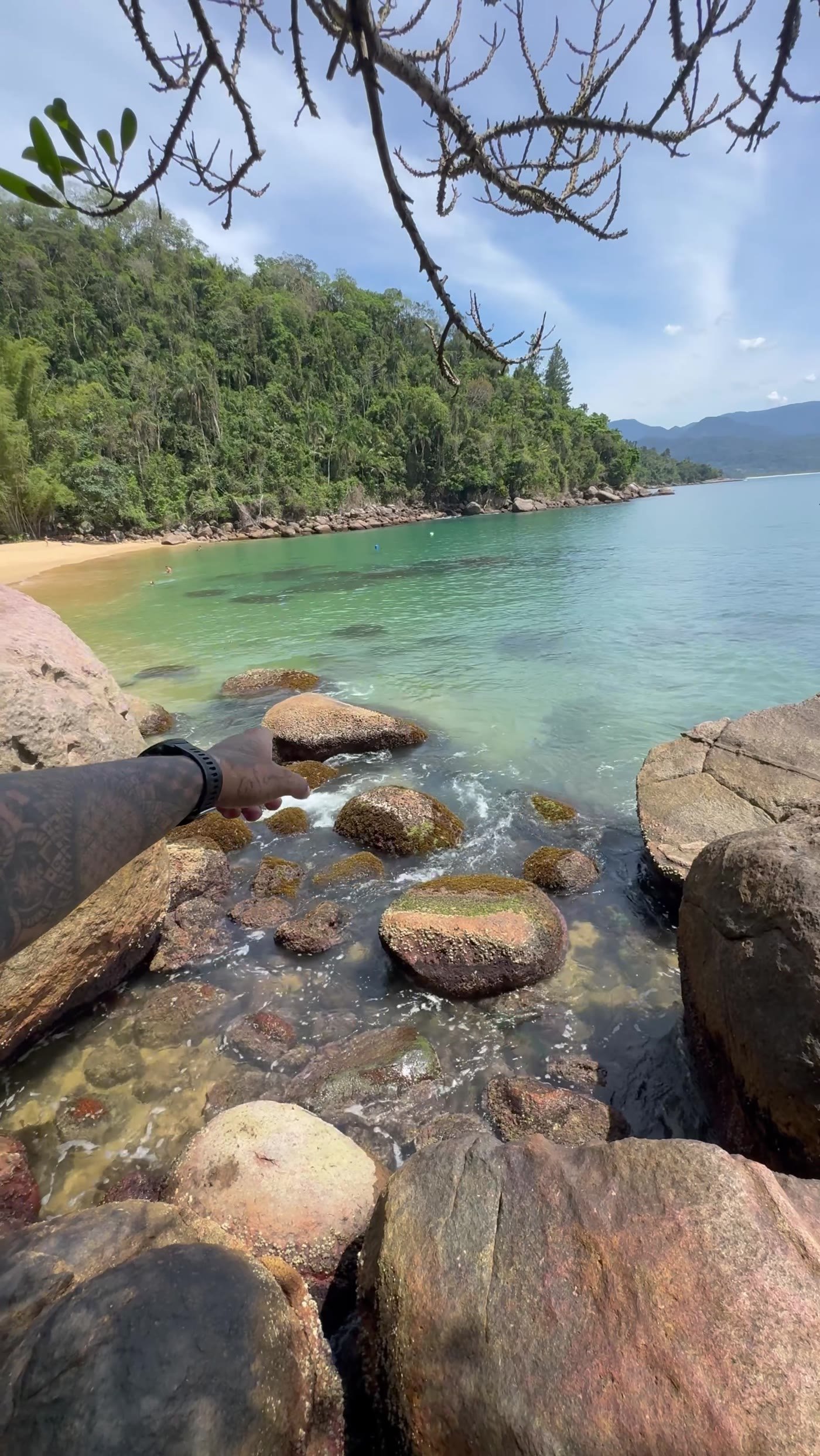 Costeira de pedras e enseada de mar calmo com mata atlântica ao fundo